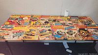 Collection of 19 vintage comic books laid out on a table with titles Hot Rods, Schwinn, Speed Demons, Dick Tracy, Dan'l Boone, Tomahawk, Outlaw Kid, Teenage Hotrodders visible in good condition.
