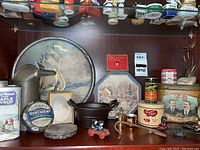 Display of various vintage tins, small cast iron Amish figures, and metal coasters arranged on shelf