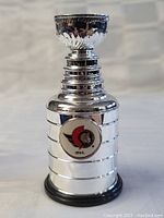 Full view of the silver-colored miniature Stanley Cup replica with black base and Ottawa Senators logo.