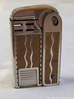 Close-up photo of the antique pocket lighter showing the front with wavy line decorations and ignition area.
