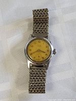 Antique Telix wristwatch with yellowed dial and metal band showing wear.