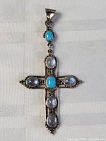 Front view of large sterling silver cross pendant with turquoise and moonstone stones on white cloth background.