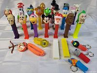 Group photo showing 17 PEZ dispensers with different character heads including Santa Claus, Mickey Mouse, Kermit the Frog, Chewbacca, and others, along with some PEZ accessories placed on a table.