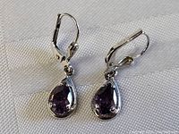 Both earrings showing teardrop-shaped purple amethyst stones set in sterling silver with lever-back closures.