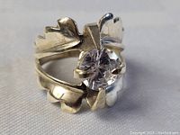 Close-up front and side view of the sterling silver ring with a clear round cut stone centered in prong setting. Shows the band design and stone clarity.