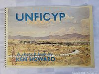Front cover of spiral-bound sketchbook titled 'UNFICYP' featuring a detailed watercolor landscape by Ken Howard.