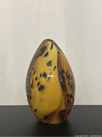 Front view of an egg-shaped amber glass paperweight with black speckles and smooth finish.