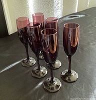 Front view of six amethyst-colored champagne flutes showing their slender stems and elongated bowls.
