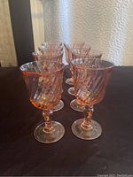 Set of eight pink swirl vintage wine glasses arranged on a dark surface.