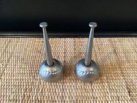 Two metallic baseball bat and ball-shaped pen holders standing upright.