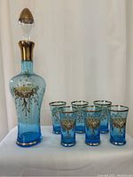 Photo showing decanter with stopper and six matching blue glasses against a white background.