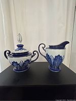 Photo of the vintage Bombay Company creamer and sugar set on black surface against light background showing the full set of two pieces with cobalt blue and white botanical pattern and platinum details.