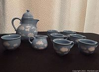 Photo showing complete cloud-themed coffee and tea set including pot, sugar bowl, creamer and six cups on black surface