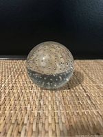 Side view of one clear glass sphere paperweight showing rectangular shape bubbles inside.