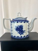 Front side of vintage floral flow blue teapot with blue floral patterns and ornamental border on white base, showing geometric finial on lid and angular handle.