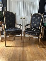 Photo showing front of the pair of gold vintage armchairs with black and gold Fleur de Lys upholstery.