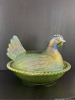Front and side angled view of green carnival glass hen on nest with iridescent finish and detailed feathers.