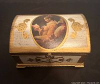 Top view of the domed lid showing the painted image of a woman reading, gold decorative appliques on cream background with gold accents.