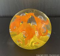 Clear glass floral paperweight with yellow and orange flowers and controlled bubbles shown from the side.