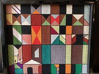 Front view of mid-century modern geometric stitchwork textile art in frame, showing colorful abstract shapes including house and figures.