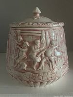 Front side of the pink glazed ceramic cookie jar showing detailed embossed figures including a witch and tavern characters, with a finial lid and decorative border.