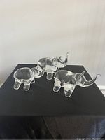 Three clear crystal elephant figurines viewed from side angle showing different poses on black fabric background.
