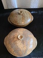 Two speckled ceramic pots with lids and handles on a black surface.