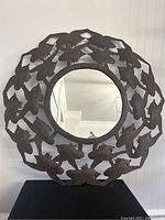 Full front view of the 24-inch round mirror showing the metal bird design frame and reflective glass center.