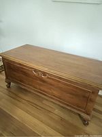 Front view of the vintage wooden chest showing carved details and bun feet.