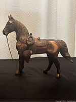 Full side view of vintage copper horse figurine showing body, saddle, and chain bridle.