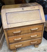 Front view of the vintage wooden drop front desk showing three drawers and hinged drop front panel with wood grain and handles.