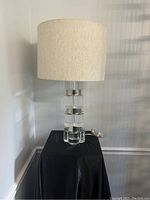 Full view of vintage lucite table lamp with beige fabric drum lampshade on black covered stand.