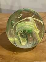 Close-up photo of a handblown glass paperweight showing yellow and green swirl inside a clear sphere with visible air bubbles.