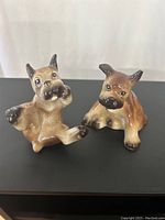Front view of two ceramic boxer dog salt and pepper shakers sitting side by side on a dark surface against a white background.