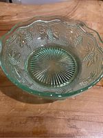 Top-down view showing the scalloped edge, textured grape clusters, leaves, and starburst base pattern of the green uranium glass bowl.