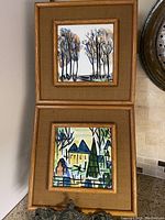 Pair of two framed hand-painted porcelain ceramic tiles displayed vertically, featuring stylized mid-century modern landscapes and trees.