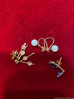 Photo showing three pairs of 14K gold earrings with different semi precious stones: blue round stones, clear faceted crystals, and blue faceted stud stones on a red background.