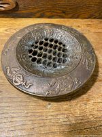 Top view showing perforated center and intricate Asian motifs including animals and calligraphy around the top edge.