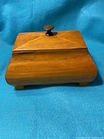 View of the wooden box with carved lid and knob, and smooth polished wooden surface.