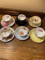 Overview of all six vintage china cups and saucers on wooden surface.