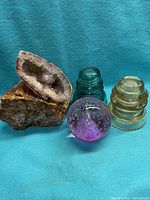 Photo showing all five items: two vintage insulators, petrified wood, amethyst geode, and purple glass paperweight against blue cloth background.
