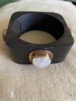 Front angle view of a square, dark rosewood bangle with a rounded inner edge. One visible side shows a circular moonstone cabochon set in a round metal bezel.
