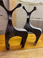 Two black metal minimalist elk sculptures on wooden surface against concrete block wall