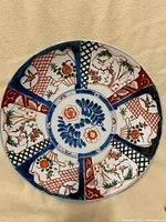 Full view of the vintage hand-painted Asian porcelain plate showing multicolored floral and nature motifs in segmented panels around a central floral design.