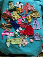 Full view of the vintage Barbie clothing lot arranged on a turquoise blanket, showing a mix of tops, bottoms, and dresses.