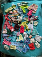 Full lot of mixed vintage Barbie clothing pieces laid out on blue background, showing variety including dresses, pants, skirts, tops, and accessories.