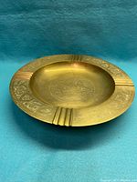 Side angled view of vintage brass ashtray showing ornate engraved Middle Eastern design and grooved cigarette rests.