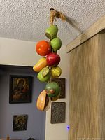 Large hanging ceramic fruit assortment displayed hanging near ceiling, visible fruits include green pears, an orange, a red apple, and a mango.