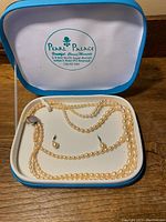 Blue Pearl Palace box containing the 3-string pearl necklace and matching pearl stud earrings inside with lid open showing branding.