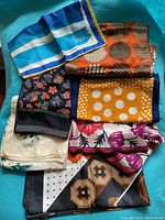 Top view of 7 vintage silk scarves folded together showing diverse color schemes and patterns like florals, polka dots, geometric shapes, and color blocking.